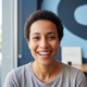 A happy woman in her late 30s smiles warmly, looking at the camera. The background is a soft blend of slate blue and bright w