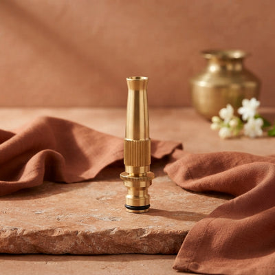 A high-pressure brass nozzle placed on a textured terracotta surface with burnt sienna fabric and bright white lighting.